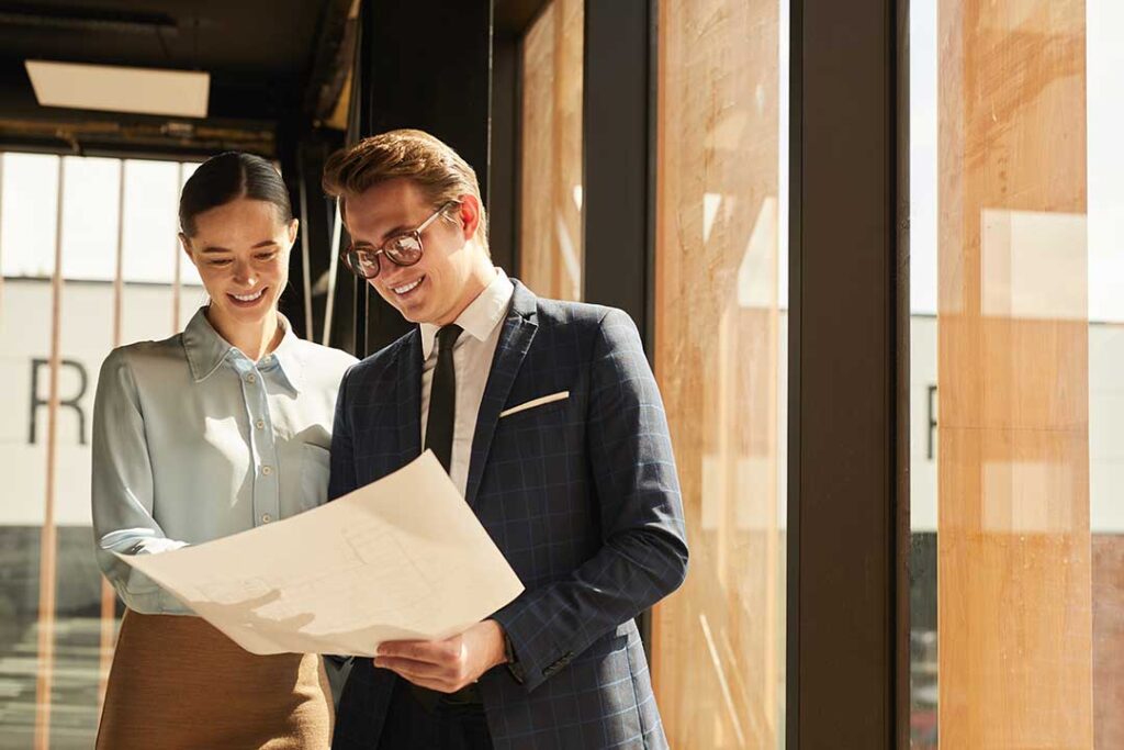 A couple reviews paperwork with a real estate agent at a kitchen table filled with documents and coffee cups.