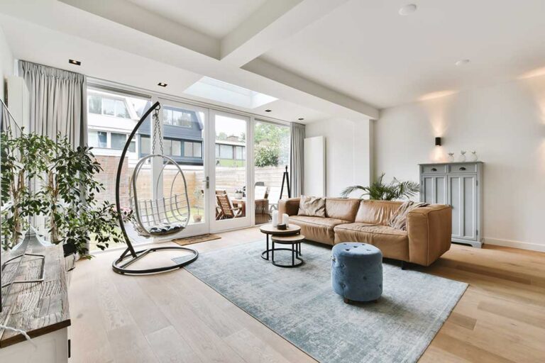 A couple reviews paperwork in a sunlit living room filled with moving boxes and a 'For Sale' sign visible outside.